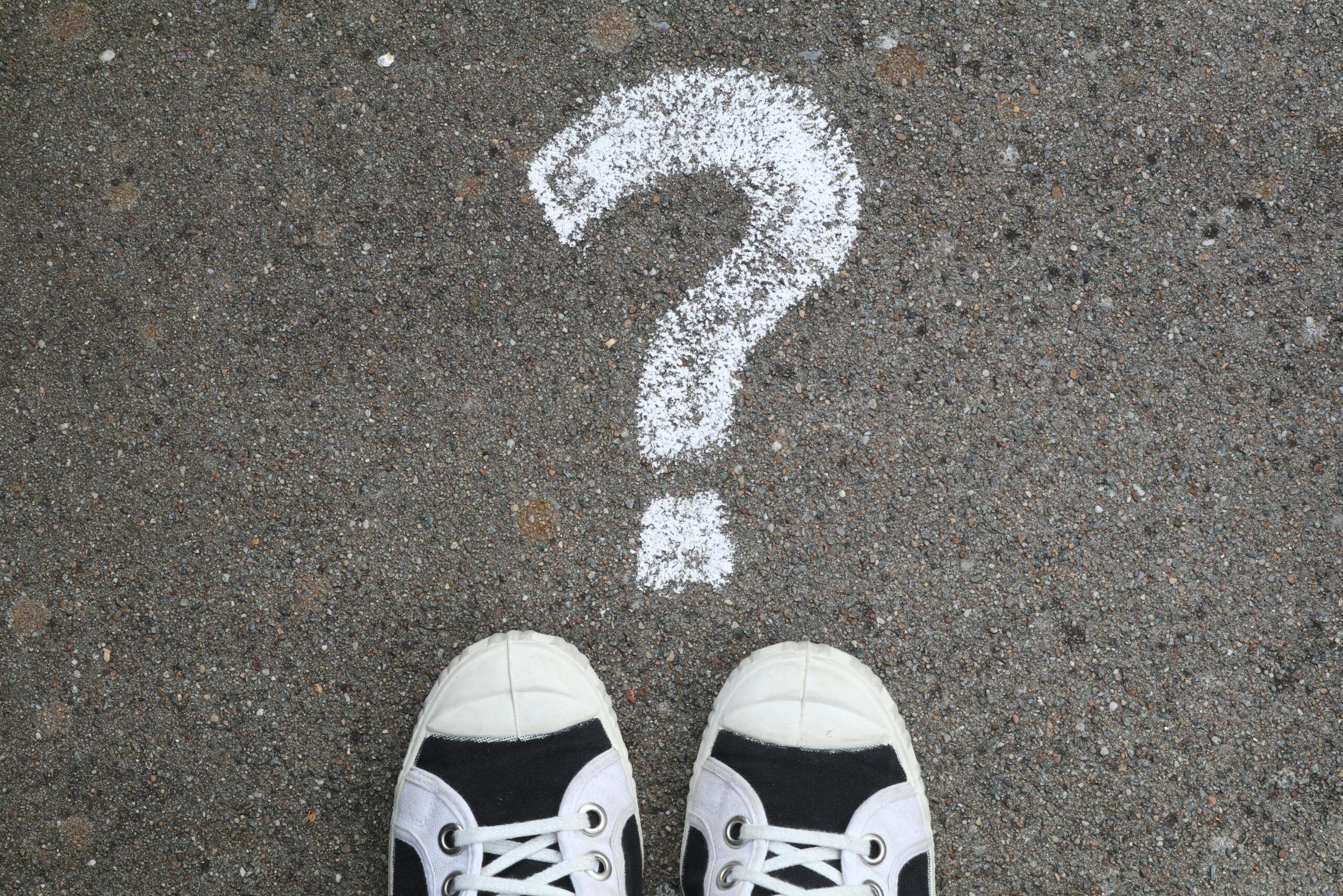 Home Sneakers on pavement with a chalk question mark, symbolizing curiosity or decisions.